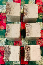 Image of 6 white soap squares with herbs on top sitting on a green and red checkered table cloth.